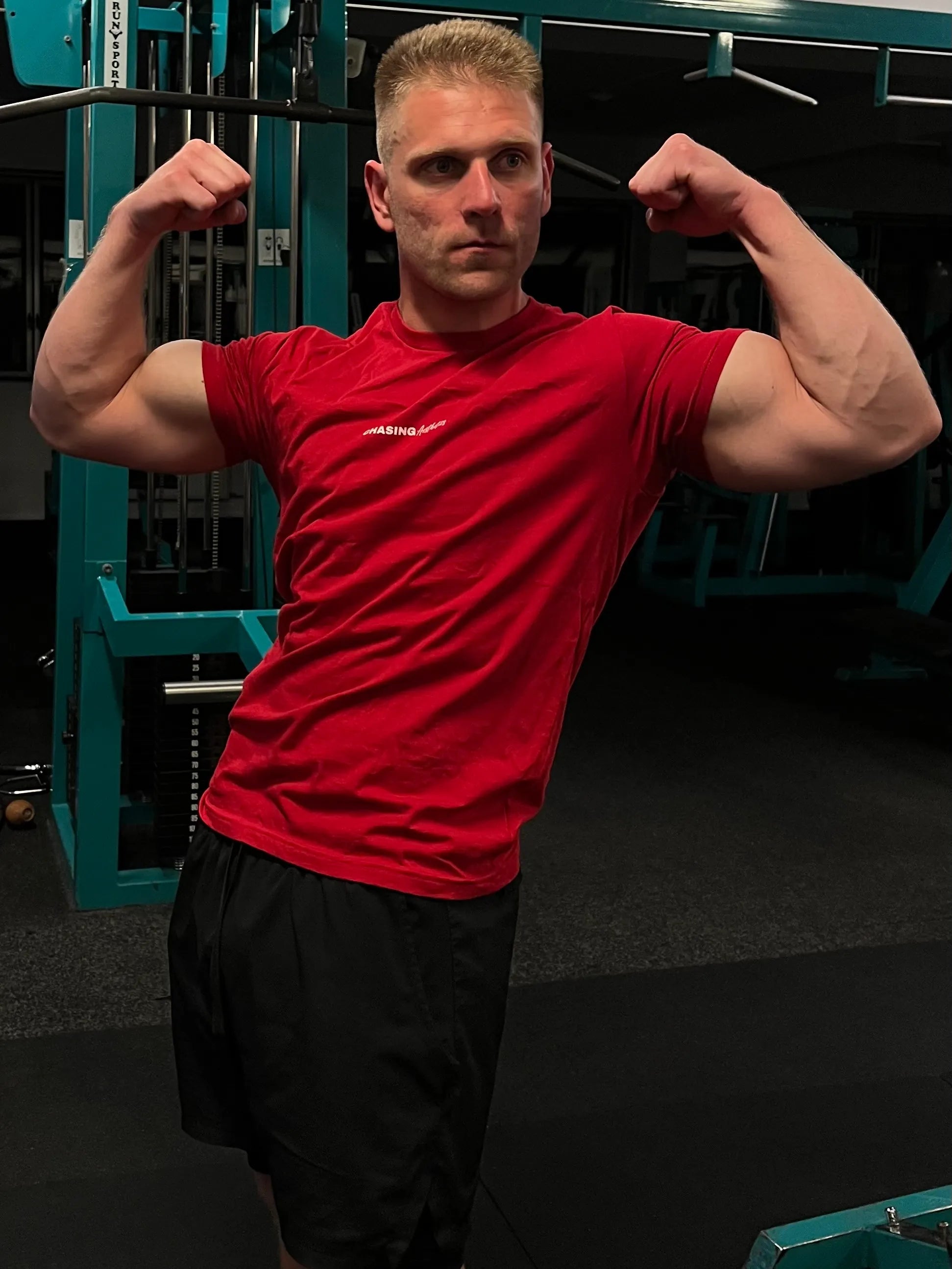 Man in a red shirt flexing muscles in a gym setting