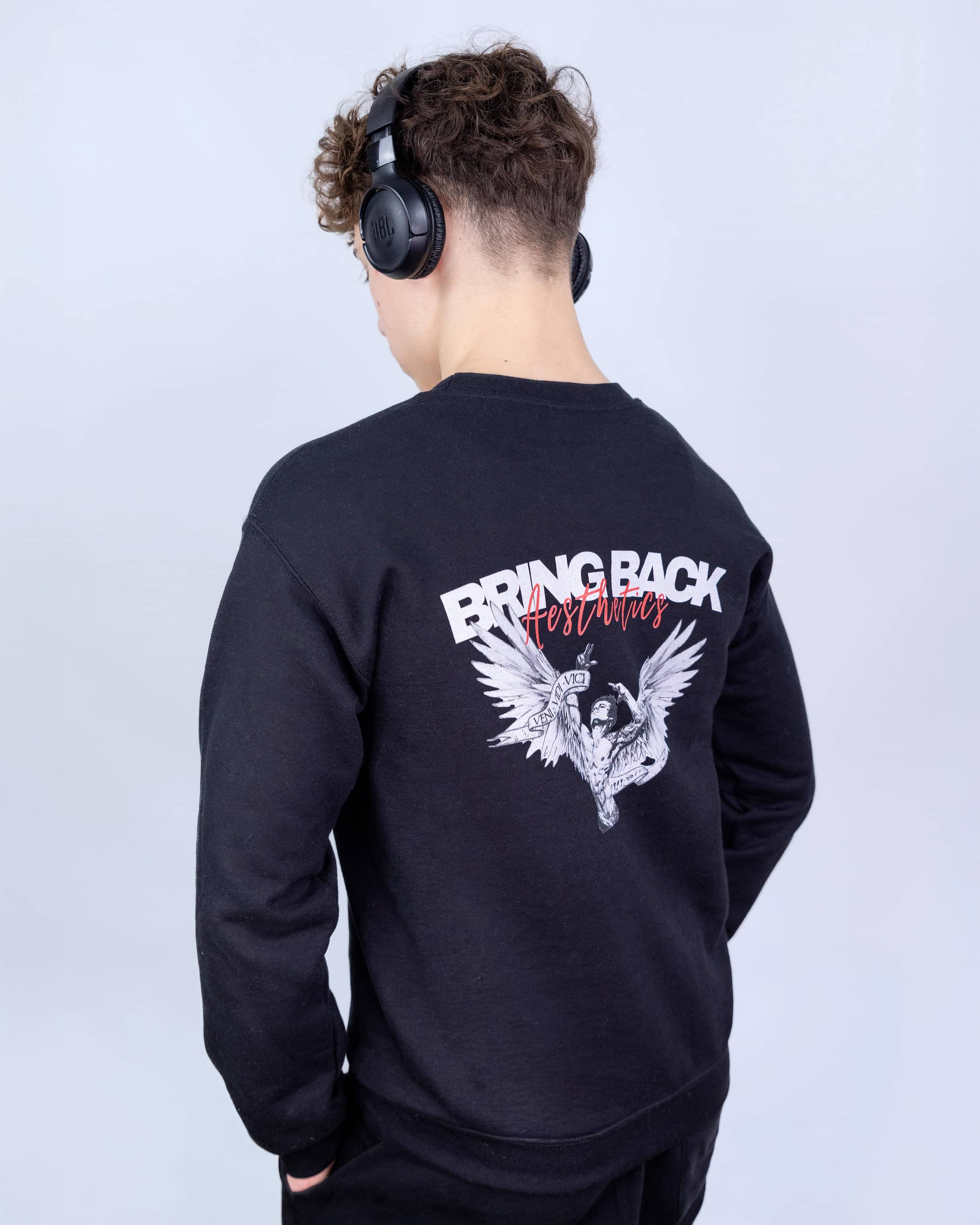 Person wearing a black sweatshirt with a design and text on the back, standing against a light gray background.