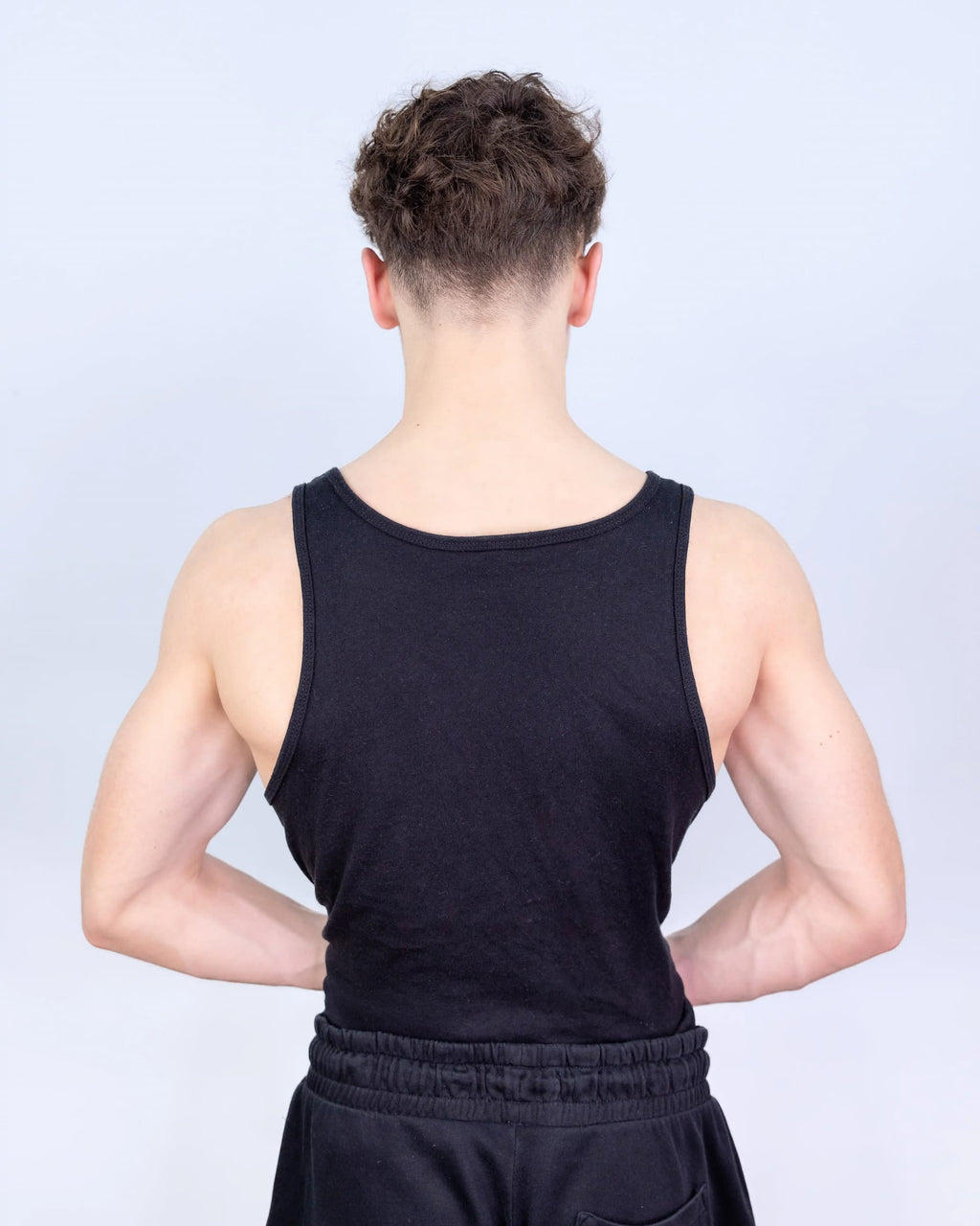 Person wearing a black tank top and dark shorts against a light gray background
