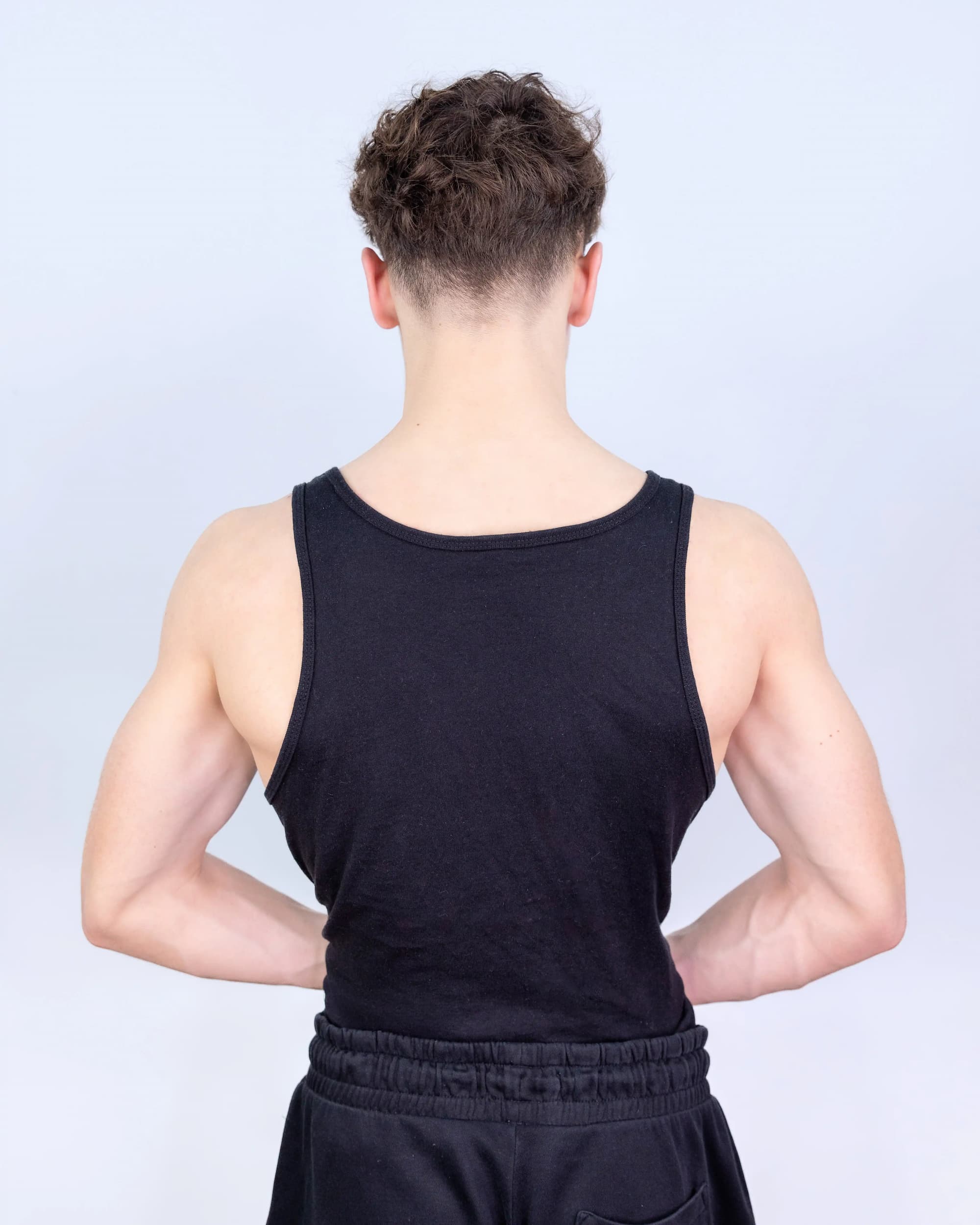 Person wearing a black tank top and dark shorts against a light gray background