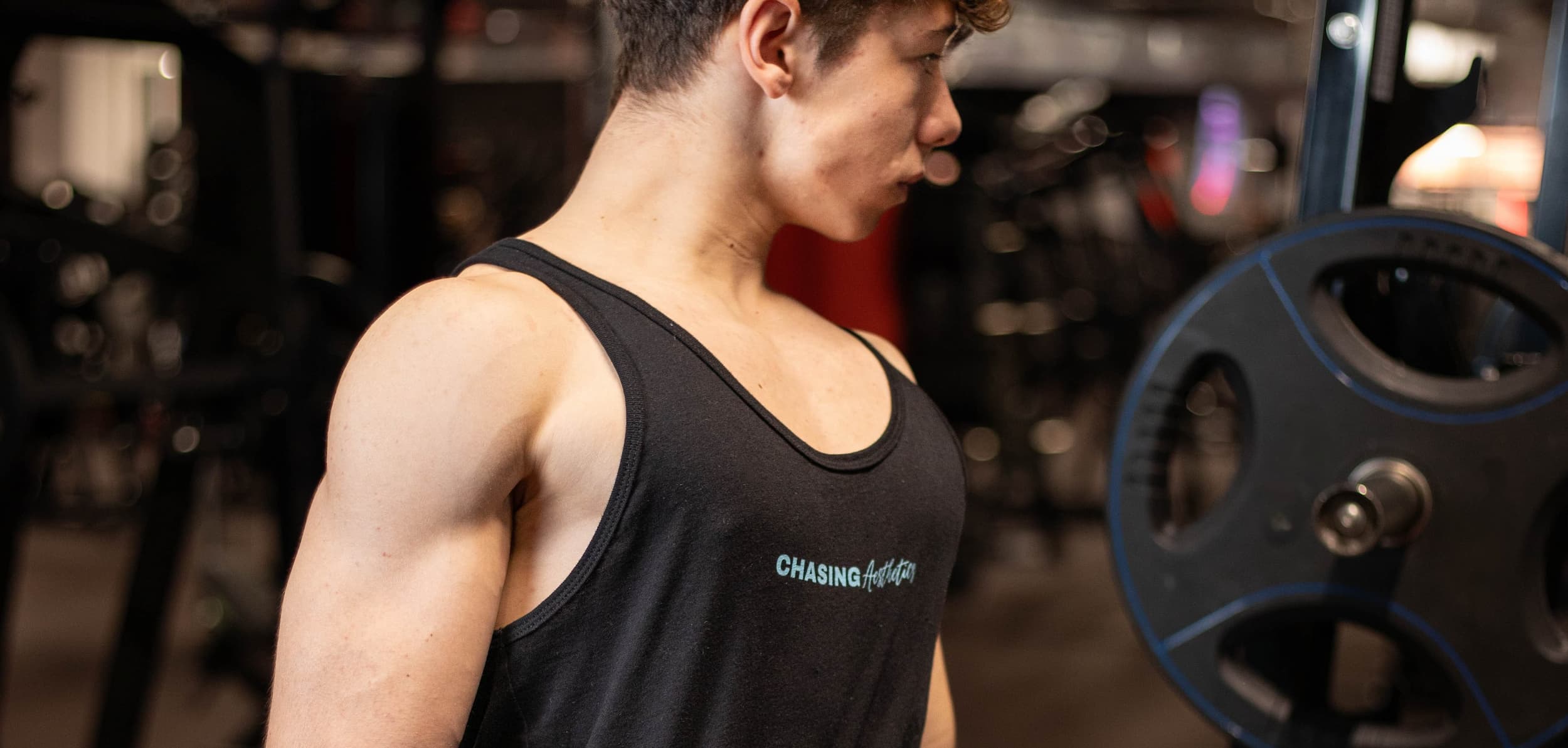 Person wearing a black tank top with 'Chasing Aesthetics' logo in a gym setting